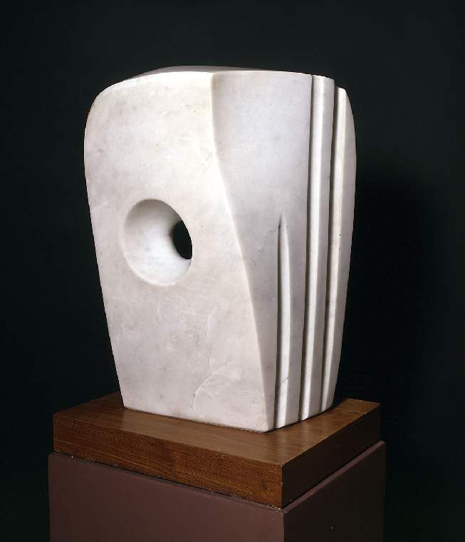 A photograph of a sculpture called Minoan Head made by Barbara Hepworth. It is a tall white marble abstract sculpture with a hole in the middle, going all the way through. The shape is like a cuboid in shape, with rounded edges. The right side has three lines carved into it, perpendicular coming down.