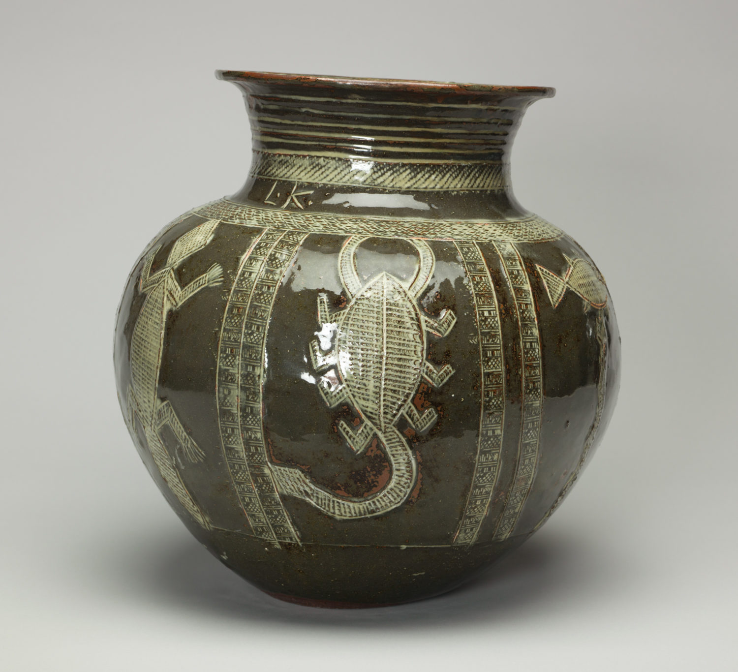 A green ceramic stoneware water jar. It is decorated with animals. This side shows a lizard, scorpion and fish.