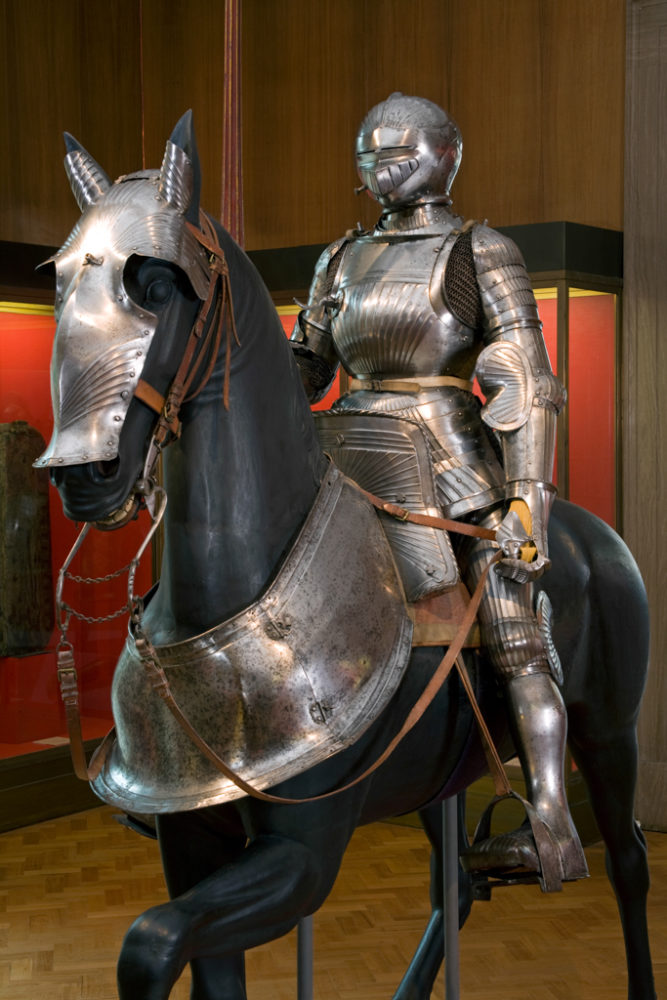 A mannequin dressed in a medieval suit of armour sits on a lifesize horse model, which is also dressd in armour