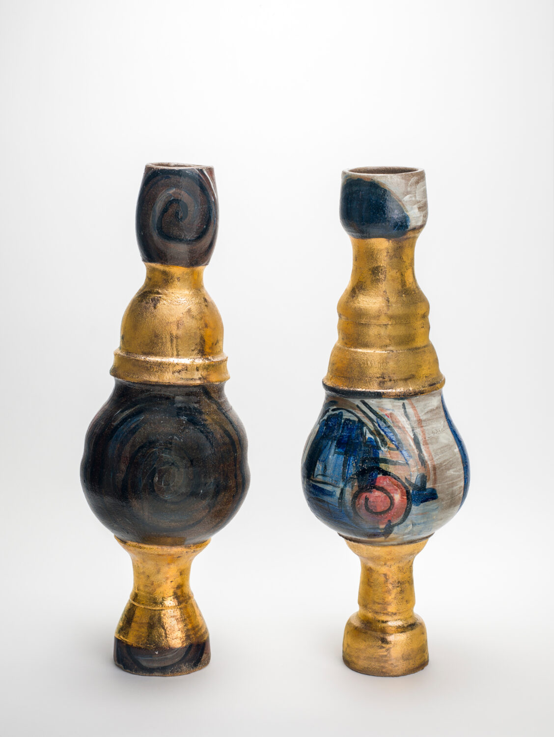 Two sculpted vessels against a white background. Both have gold features but other sections are different colours. One is brown and black and the other is blue, white and pink.