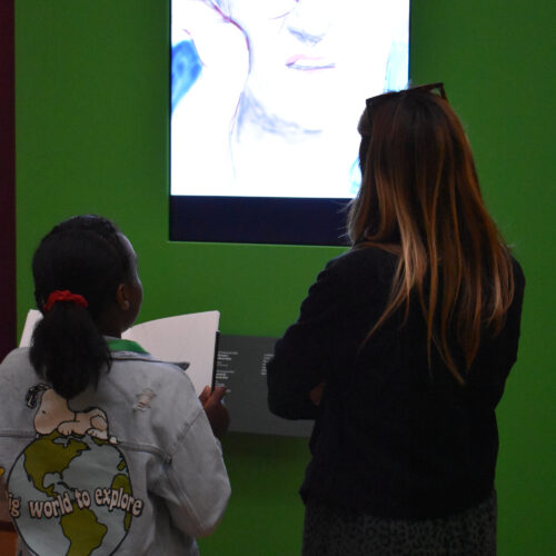 A woman and a girl look at a portrait on a screen together.