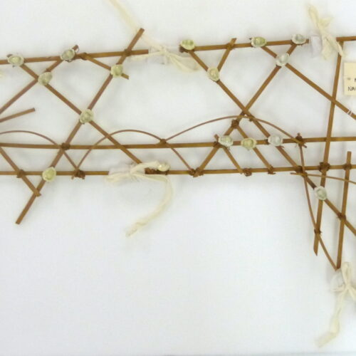 A photograph of many thin sticks of woo that have been tied together at specific points. At some points there are tiny shells on the joints, and at a few points there are ties on the sticks. Most sticks are straight but three bend across the middle at regular intervals.